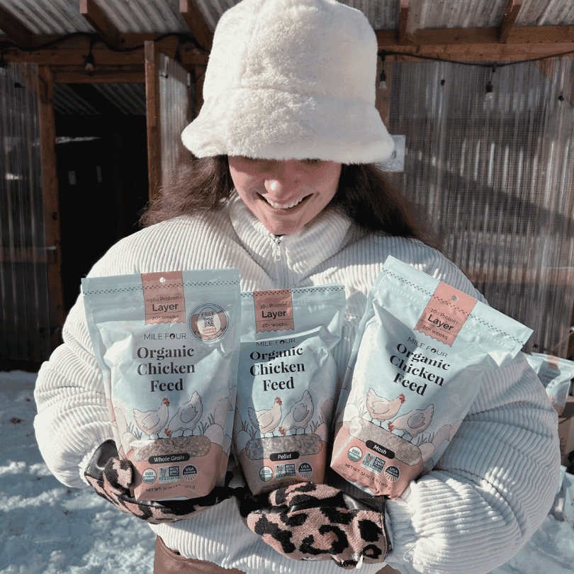 a woman holding three packs of Mile Four Layer Organic Chicken Feed