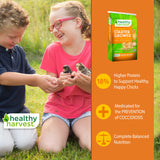 Hatching Time Healthy Harvest. Medicated Starter grower. 2 children can be seen holding baby chicks. There is a bag of feed on right side of image.