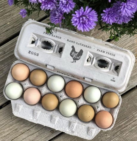 Hatching Time Henlay Egg Carton pre-marked with free range, hand gathered, farm fresh and laid local branding on table by flowers and filled with white and brown chicken eggs.