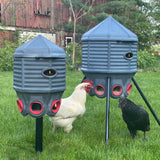 Two gray chicken feeders with red compartments on stands, with chickens interacting in a grassy area.