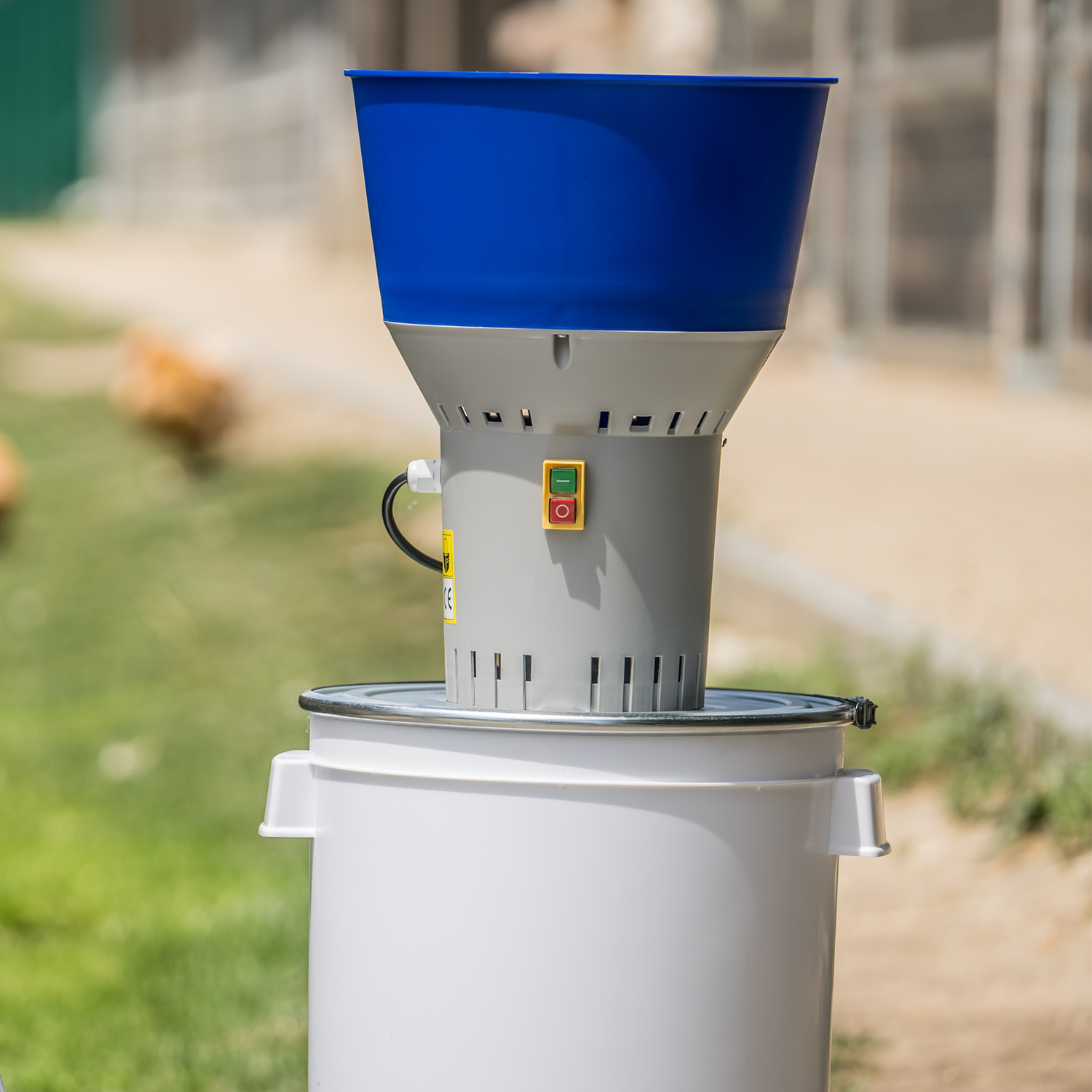 Farm Mill 50 Feed Crusher with blue hopper and white 50L plastic bucket placed outdoors on a farm for grain grinding