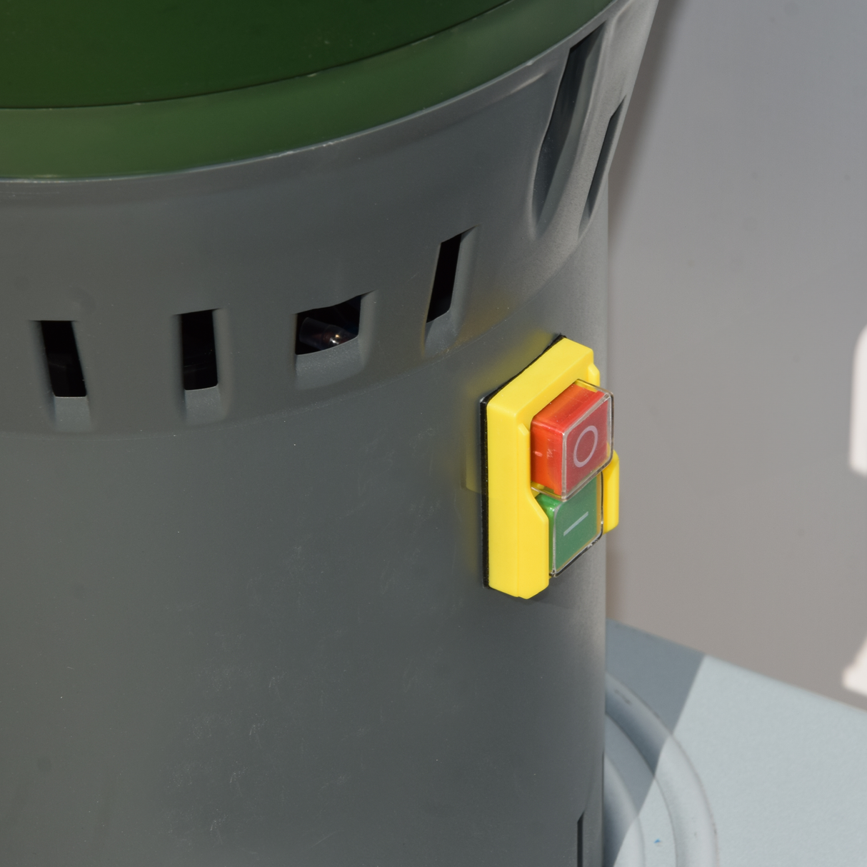 Close-up of Farm Mill Compact Feed Crusher showing red and green power switch with protective yellow frame on durable gray motor housing