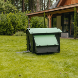 Hatching Time Nestera. Large coop can be seen in image on grass. Coop has door open with automatic coop opener. Ramp is leading up to opening for easy chicken access. Nesting box is on side connected to chicken coop, with lifting door for easy egg access. Roof of coop is slanted to prevent roosting.