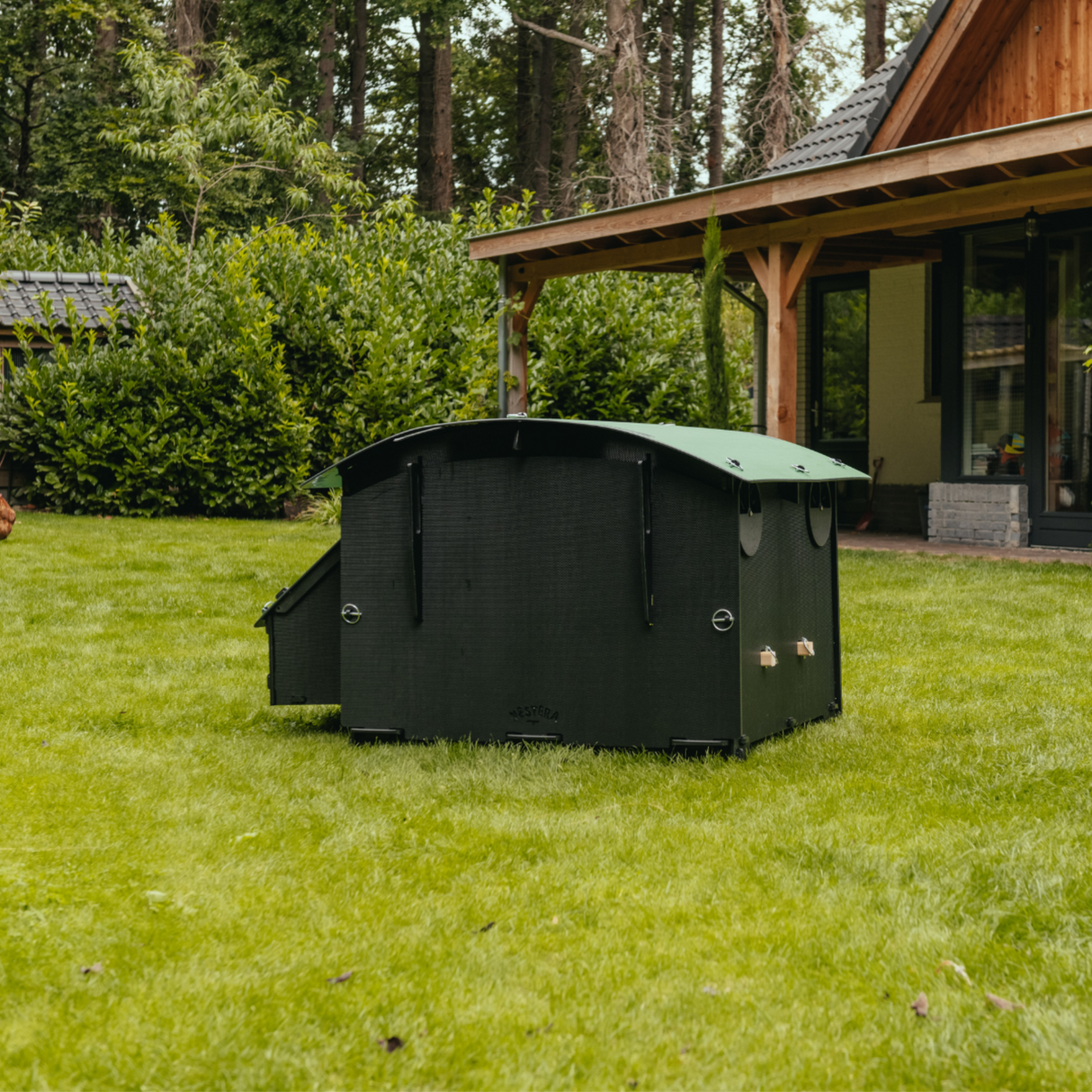 Hatching Time Nestera. Large coop can be seen in image on grass. Coop has door open with automatic coop opener. Ramp is leading up to opening for easy chicken access. Nesting box is on side connected to chicken coop, with lifting door for easy egg access. Roof of coop is slanted to prevent roosting.