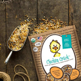 Hatching Time Treats for Chickens. Chicken Crack bag is open and laying on table. Treats are spilled out showing seeds, grains and insects that are in treats for chickens. Scoop can be seen full of chicken treats.