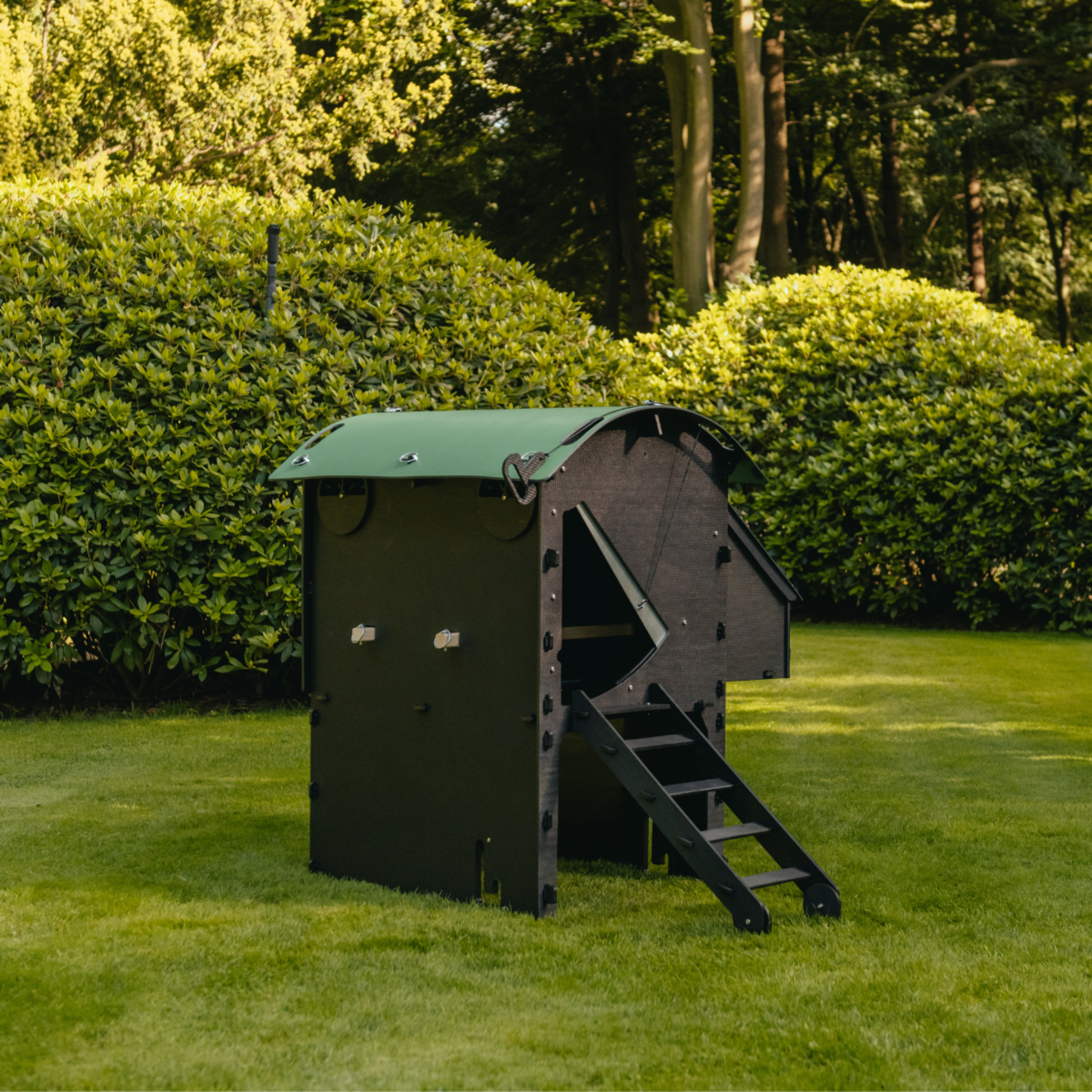 Hatching Time Nestera. Medium Raised coop can be seen in image on grass. Coop has door open with automatic coop opener. Ramp is leading up to opening for easy chicken access. Nesting box is on side connected to chicken coop, with lifting door for easy egg access. Roof of coop is slanted to prevent roosting.