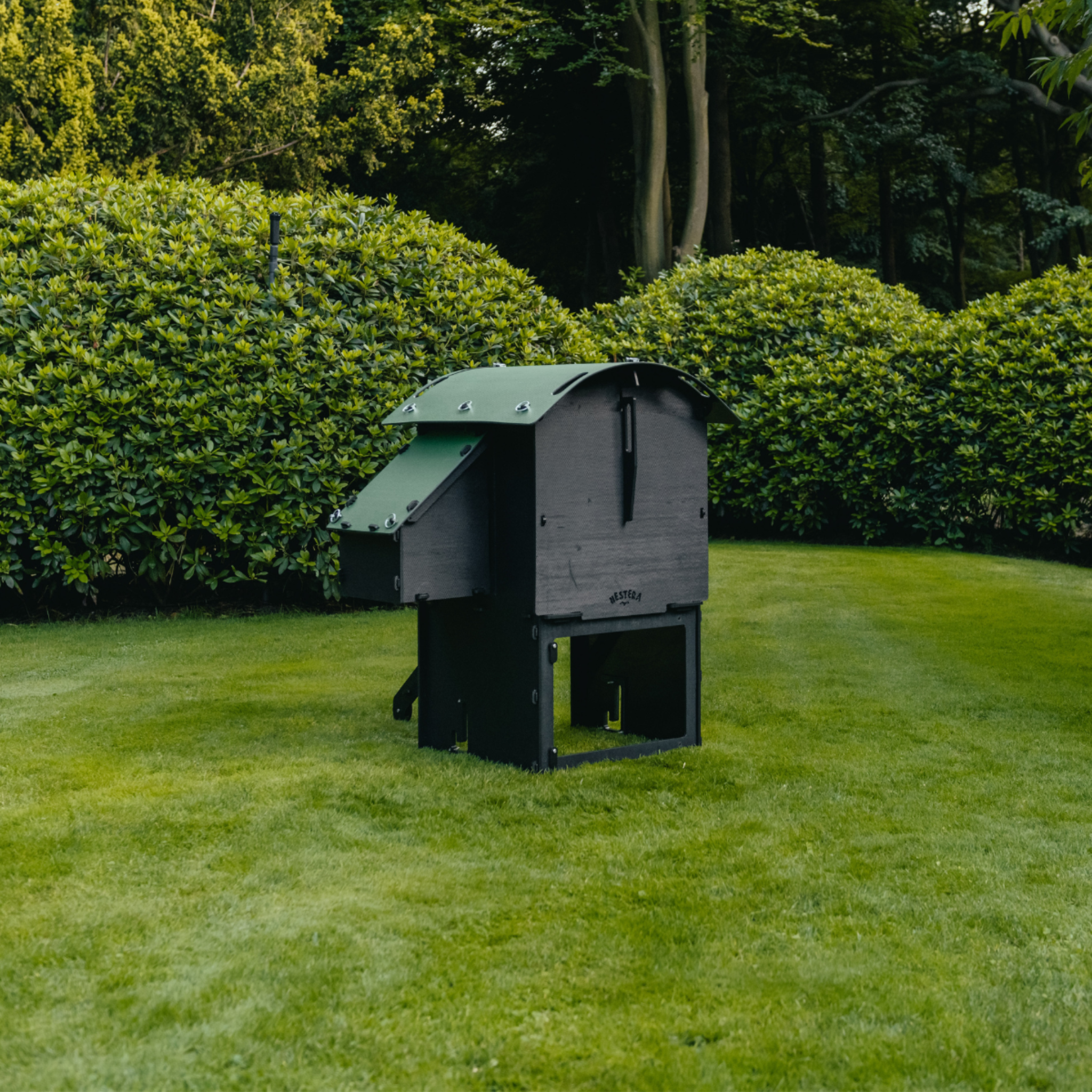 Hatching Time Nestera. Rear view raised small coop can be seen in image on grass. Nesting box is on side connected to chicken coop, with lifting door for easy egg access. Roof of coop is slanted to prevent roosting.