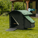 Hatching Time Nestera. Small house chicken coop can be seen in image. Coop door is open with ramp leading up to it for easy chicken access. Nesting box can be seen on side of chicken coop. Rounded roof deters roosting. 25 year warranty can be seen in image.