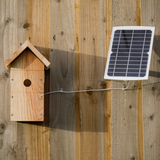 Hatching Time Nestera. Birdhouse mounted to wooden wall, solar panel mounted next to birdhouse can be seen.