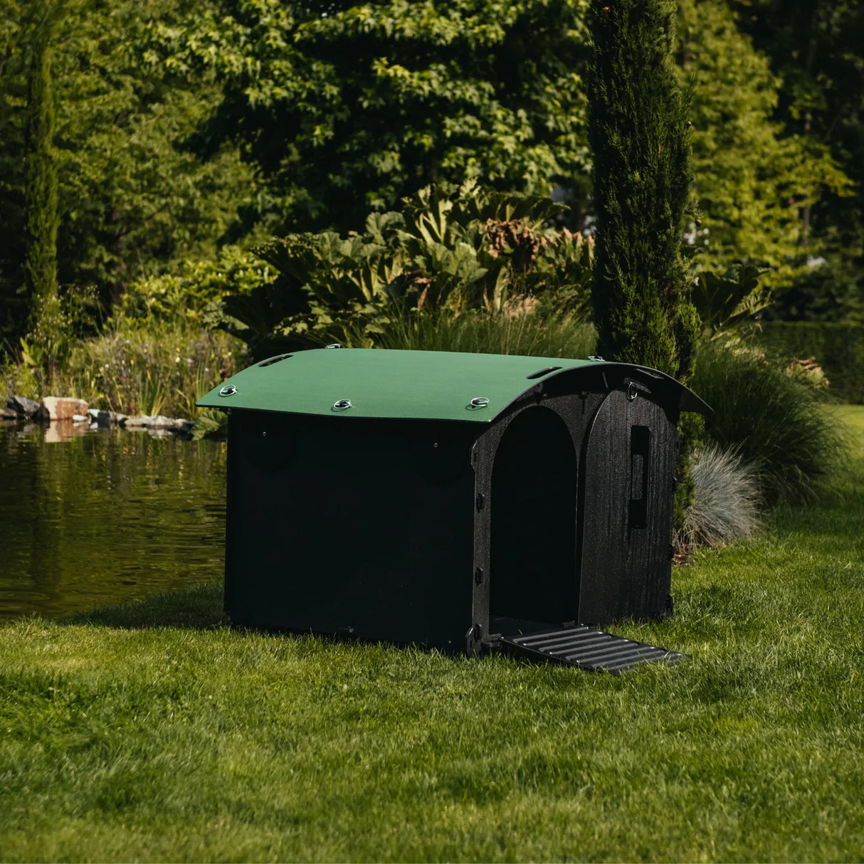 Hatching Time Nestera. Duck house can be seen in image from the front on grass. Duck house has green rounded roof, black walls and floor and walk-up ramp. Door is open.