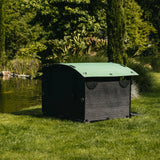 Hatching Time Nestera. Duck house can be seen in image from the side on grass. Duck house has green rounded roof, black walls and floor and walk-up ramp. Door is open.